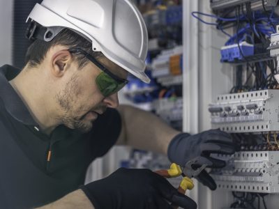 A male electrician works in a switchboard using an electrical connection cable, connecting equipment with tools.