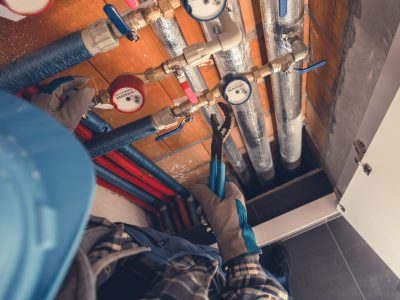 Aerial View of Plumber with Hydraulic Key Performing Hot and Cold Water Meters Service and Repair. Residential Water Supply Theme.